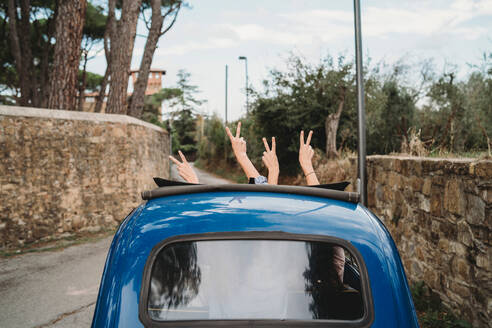 Freunde gestikulieren das Friedenszeichen im Schiebedach eines Autos, Florenz, Toskana, Italien - CUF51412