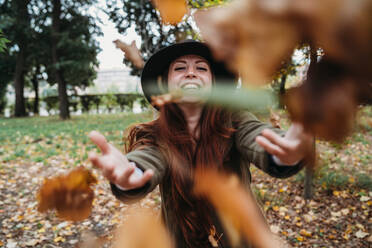 Young woman with long red hair throwing autumn leaves in park - CUF51425