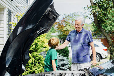 Caucasian grandfather and grandson repairing car in driveway - BLEF07546