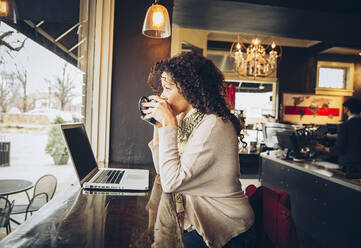 Frau benutzt Laptop und trinkt Kaffee in einem Cafe - BLEF07552