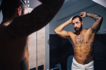 Mittlerer erwachsener Mann mit Tattoos kämmt Haare am Badezimmerspiegel, Spiegelbild - ISF21448
