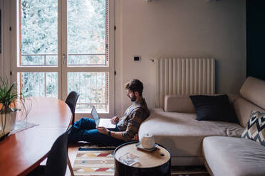 Mid adult man sitting on living room floor using laptop - ISF21460