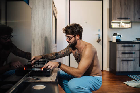 Mittlerer erwachsener Mann mit Tätowierungen spielt Vinyl auf einem Plattenspieler - ISF21464