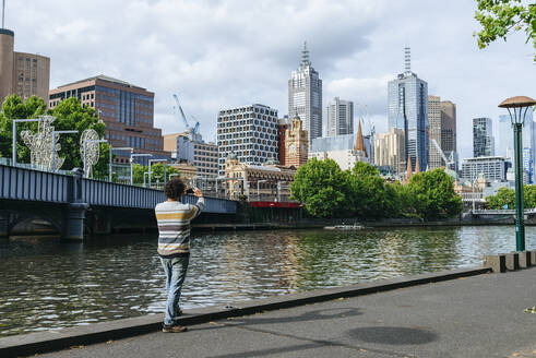 Man taking a picture of cityscape of Melbourne with Yarra river, Victoria, Australia - KIJF02492
