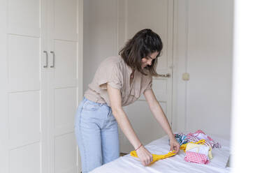 Young woman placing clothes on bed - AFVF03285