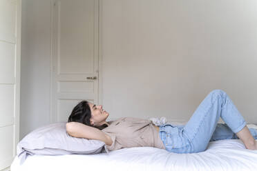 Happy young woman lying on bed with closed eyes - AFVF03301