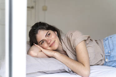 Smiling young woman lying on bed - AFVF03303