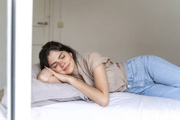 Smiling young woman lying on bed with closed eyes - AFVF03304