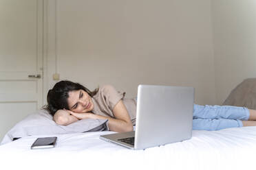 Lächelnde junge Frau auf dem Bett liegend mit Smartphone und Laptop - AFVF03305