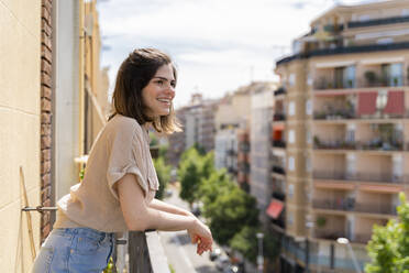 Glückliche junge Frau steht auf einem Balkon in der Stadt - AFVF03309