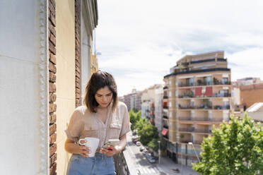 Junge Frau auf einem Balkon in der Stadt, die ein Mobiltelefon benutzt - AFVF03310