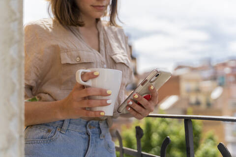 Nahaufnahme einer Frau auf einem Balkon in der Stadt mit Kaffeetasse und Mobiltelefon, lizenzfreies Stockfoto