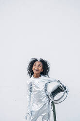 Porträt eines verblüfften kleinen Mädchens im Raumanzug vor weißem Hintergrund, das nach oben schaut - JCMF00064