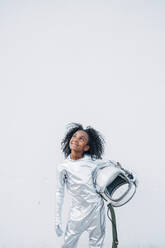 Portrait of smiling little girl wearing space suit in front of white background looking up - JCMF00065