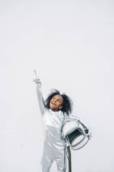 Portrait of smiling little girl wearing space suit in front of white background looking up - JCMF00066
