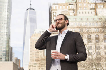 Smiling young businessman with coffee to go on the phone, New York City, USA - MFRF01304