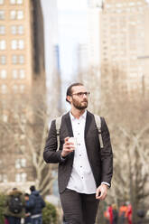 Porträt eines bärtigen jungen Geschäftsmannes mit Rucksack und Kaffee zum Mitnehmen, New York City, USA - MFRF01309