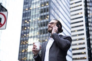 Glücklicher junger Geschäftsmann mit Kaffee zum Mitnehmen am Telefon, New York City, USA - MFRF01312