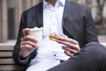 Geschäftsmann hält Donut und Kaffee zum Mitnehmen in den Händen, Nahaufnahme - MFRF01314