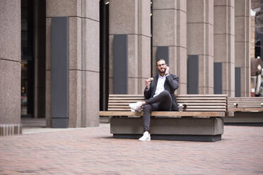 Businessman on the phone sitting on bench eating doughnut, New York City, USA - MFRF01315
