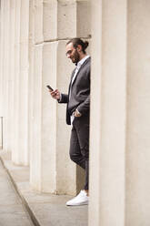 Young businessman standing among columns of Stock Exchange looking at cell phone, New York City, USA - MFRF01321