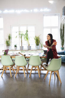 Frau sitzt auf einem Tisch in einem modernen Büro - FKF03351