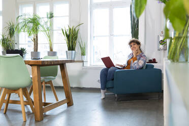 Smiling woman using laptop in armchair in office - FKF03373