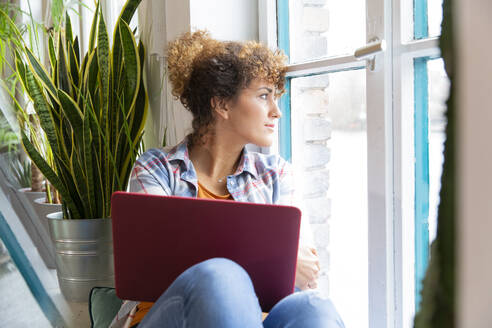 Frau mit Laptop schaut aus dem Fenster im Büro - FKF03376