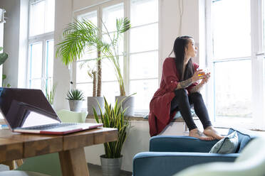 Woman looking out of window in office - FKF03379