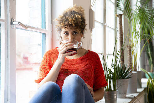 Portrait of woman drinking coffee at the window in office - FKF03397