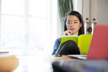 Woman working at table in office reading a book - FKF03402