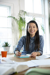 Portrait of happy woman working at table in office - FKF03405