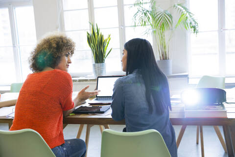 Rückansicht von zwei Frauen, die in einem modernen Büro mit Videoprojektor auf dem Tisch arbeiten, lizenzfreies Stockfoto