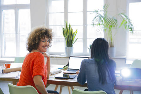 Lächelnde Frau mit Kollege in modernem Büro mit Videoprojektor auf dem Tisch, lizenzfreies Stockfoto