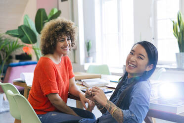 Two happy women in modern office with video projector on table - FKF03413