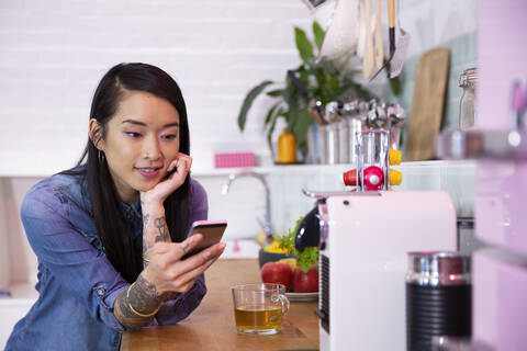Frau mit Handy und Tee in der Büroküche, lizenzfreies Stockfoto