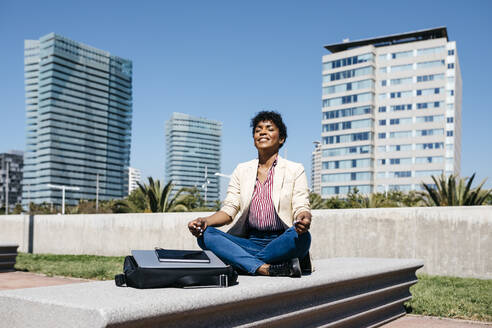 Geschäftsfrau sitzt auf einer Bank und meditiert - JRFF03297