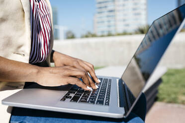 Businesswoman sitting on bench and using laptop in the city - JRFF03309