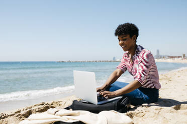 Woman sitting on the beach while working with the laptop - JRFF03319