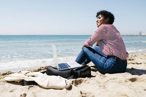 Frau sitzt am Strand und arbeitet mit dem Laptop - JRFF03321