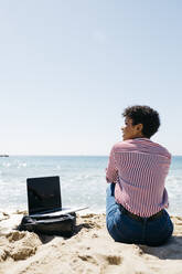 Frau sitzt am Strand und arbeitet mit dem Laptop - JRFF03322