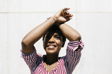 Portrait of woman covering the sun with her arm, white wall in the background - JRFF03332