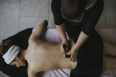 Young woman with sachets on her back during stamp massage - OCAF00415