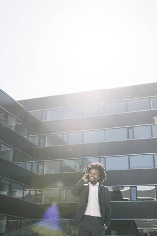 Lächelnder Geschäftsmann, der vor seinem Büro mit einem Handy telefoniert, lizenzfreies Stockfoto