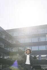 Smiling businessman talking on cell phone outside office - AHSF00539