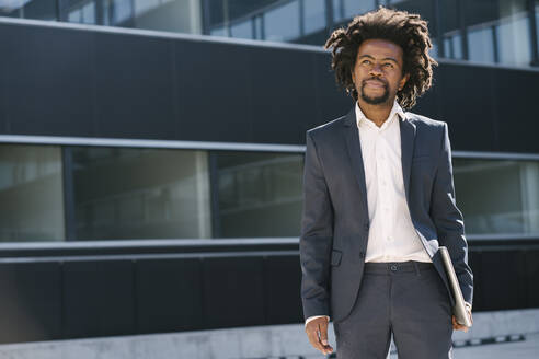 Businessman holding laptop outside office - AHSF00563