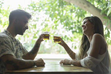 Glückliches junges Paar stößt am Tisch eines Restaurants mit Biergläsern an - JPTF00171