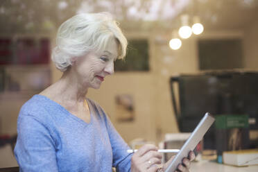 Lächelnde reife Frau hinter Fensterscheibe mit digitalem Tablet - PNEF01692