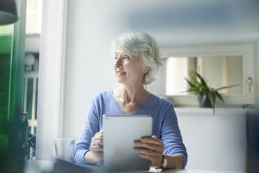 Smiling mature woman with digital tablet looking out of window - PNEF01695