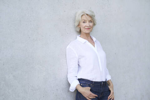 Portrait of relaxed mature woman wearing white shirt leaning against concrete wall stock photo